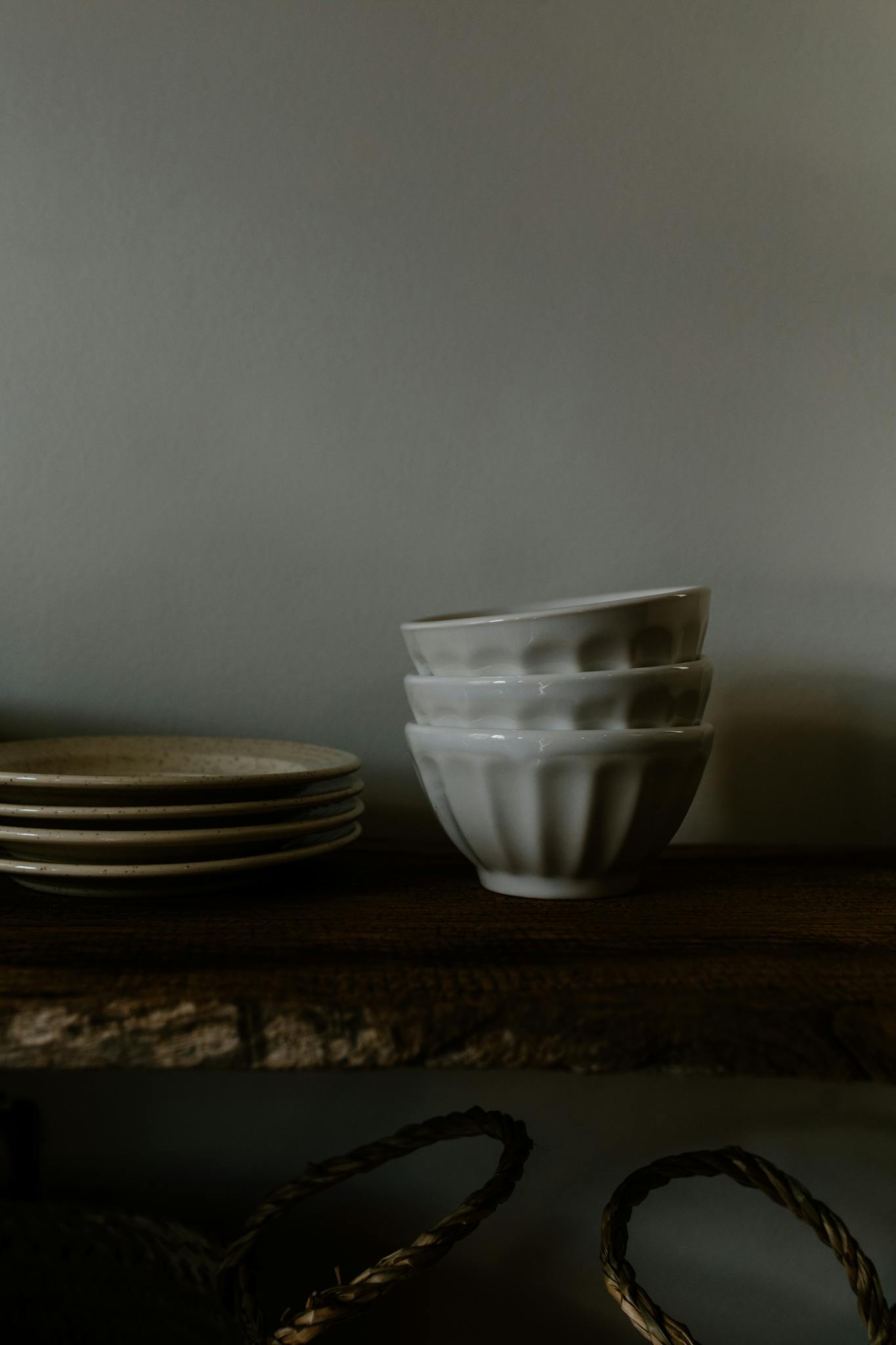 A stylish arrangement of white ceramic bowls and plates on a rustic wooden shelf in a dimly lit room.