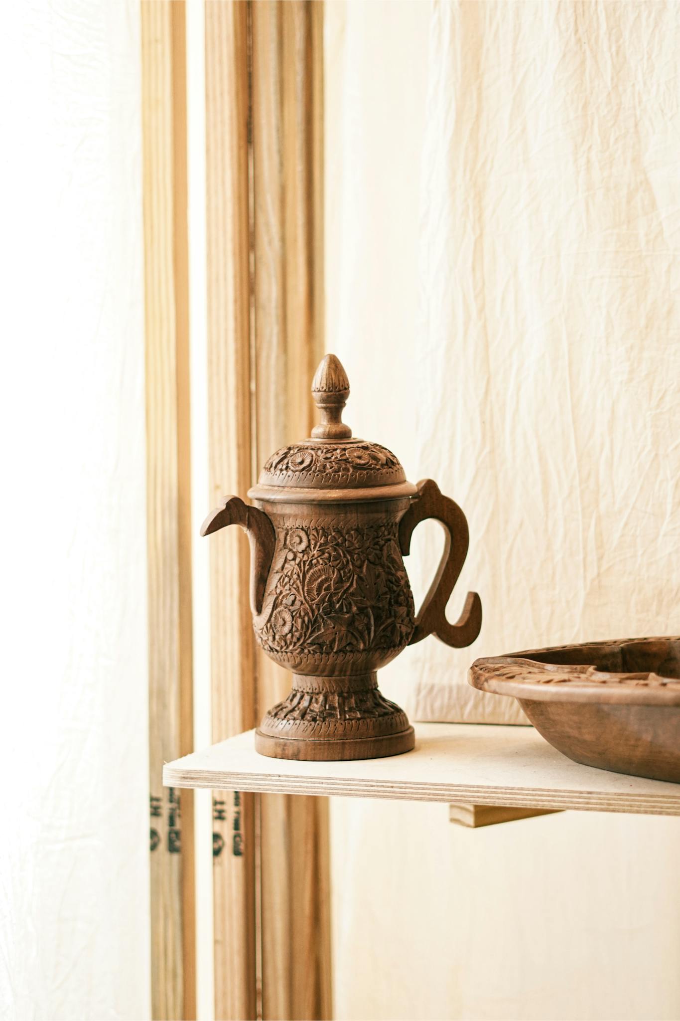 Intricately carved wooden teapot displayed on a shelf, highlighting craftsmanship.